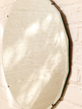 Load image into Gallery viewer, An octagonal wall mirror with a dark metal frame mounted on a white brick wall, reflecting soft light and shadows.
