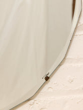 Load image into Gallery viewer, A close-up of a large, curved mirror with a silver metal frame, mounted on a textured off-white brick wall.