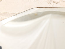 Load image into Gallery viewer, Close-up of a white ceramic or porcelain surface with a glossy curved edge and a textured beige background.