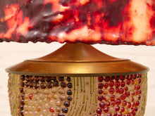 Load image into Gallery viewer, Close-up of a decorative table lamp with a textured red and amber glass shade and a patterned beige and red beaded base.