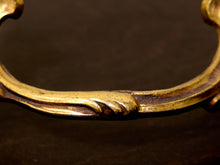 Load image into Gallery viewer, Close-up of an ornate antique-style brass drawer pull handle with a curved, decorative scrollwork design, set against a dark brown background.