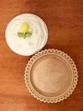 Load image into Gallery viewer, A ceramic lemon-themed dish set on a warm brown wooden background, featuring a round white plate with a swirled top and a small green lemon decoration, alongside a matching scalloped beige plate below.