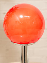 Load image into Gallery viewer, A glossy translucent orange-red spherical lamp shade mounted on a polished silver metal stem, shown against a softly blurred light beige background.