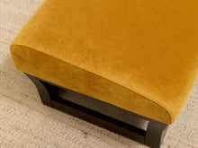Load image into Gallery viewer, A mustard yellow velvet ottoman with a dark wood base, shown in a close-up view on a textured beige rug.