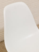 Load image into Gallery viewer, Close-up of a glossy white molded chair seat against a light brick wall and beige carpet.