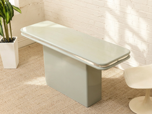 Load image into Gallery viewer, A modern bench with a glossy pale sage green top and a matte matching base, styled in a bright room with a white brick wall, beige carpet, a potted plant, and a white tulip chair.