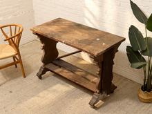 Load image into Gallery viewer, Antique Victorian carved wood pedestal table with thick rectangular top, sculptural central base, aged brown finish, and caster wheels.