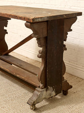 Load image into Gallery viewer, An antique dark brown wooden console table with ornate carved legs and casters, shown on a textured beige carpet against a white brick wall.