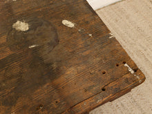 Load image into Gallery viewer, A close-up of a rustic dark brown wooden tabletop with visible grain, worn patches, and nail holes, set against a light beige carpeted floor.