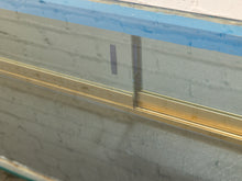 Load image into Gallery viewer, Close-up of a sliding glass door or window track system with a gold metal frame and a blue protective film on the glass.
