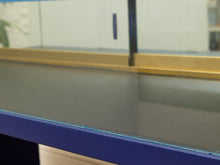 Load image into Gallery viewer, Close-up of a dark gray glass tabletop or display counter with a blue front frame and a gold horizontal trim, photographed indoors.