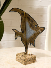 Load image into Gallery viewer, A handcrafted metal angelfish sculpture with a textured bronze finish, mounted on a square tan stone base with a small seashell, set on a light marble tabletop.