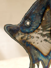 Load image into Gallery viewer, Close-up of a fish-shaped decorative glass piece with a blue, bronze, and cream iridescent glaze and water droplets, set against a soft beige background.