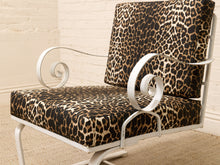 Load image into Gallery viewer, A white metal patio chair with plush seat and back cushions in a brown, black, and beige leopard print fabric, set against a light brick wall and beige rug.