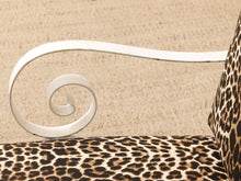 Load image into Gallery viewer, Close-up of a leopard-print upholstered chair or sofa section with a white metal scroll arm and a matching leopard-print pillow against a beige textured background.