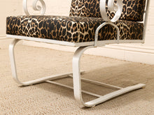 Load image into Gallery viewer, A close-up of a modern lounge chair with a white metal frame and leopard-print cushions, set on a beige textured rug against a white brick wall.