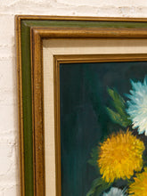 Load image into Gallery viewer, A close-up of a framed floral painting showing yellow and light blue flowers against a dark teal background, with a layered gold and green frame mounted on a white brick wall.