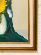 Load image into Gallery viewer, A close-up of a framed painting showing part of a yellow flower in a white vase with dark green drapery against a cream background, mounted on a white brick wall.