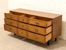 Load image into Gallery viewer, A mid-century modern wooden dresser with nine drawers, including four open drawers showing storage compartments, set against a white brick wall and beige carpet.