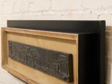 Load image into Gallery viewer, A framed black bas-relief wall art piece mounted on a light wood frame against a white brick wall.