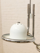 Load image into Gallery viewer, A close-up of a mid-century modern pendant light fixture featuring a glossy white ceramic dome shade and a polished chrome metal frame against a cream brick wall.