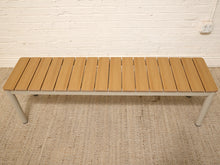 Load image into Gallery viewer, A modern outdoor bench with a light brown composite wood slatted seat and a white metal frame, shown on a textured beige rug against a white brick wall.