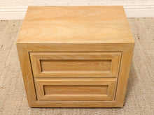 Load image into Gallery viewer, A light natural oak wood two-drawer nightstand or side table with a smooth finish and recessed drawer fronts, shown on a woven jute rug.