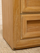 Load image into Gallery viewer, Close-up of a light oak wood furniture piece showing the corner joint and drawer front detail on a woven rug.