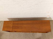 Load image into Gallery viewer, A mid-century modern wooden console table with a warm brown finish, shown from a top-down angle against a white brick wall and textured rug.