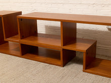 Load image into Gallery viewer, A mid-century modern wooden media console with warm brown shelving, shown against a white brick wall and beige carpet.