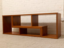 Load image into Gallery viewer, A mid-century modern wooden media console shelf with a warm cherry finish, set against a white brick wall and beige carpet.