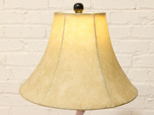 Load image into Gallery viewer, A vintage-style fabric table lampshade with a warm cream/beige color and subtle vertical seam lines, shown illuminated against a white painted brick wall background.