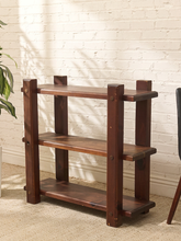 Load image into Gallery viewer, A three-tier wooden bookcase with a dark brown finish, featuring a rustic design with thick vertical posts and open shelves, set against a white brick wall.