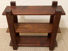 Load image into Gallery viewer, A three-tier wooden shelf with a dark brown finish, featuring thick square legs and brass-colored corner hardware, set against a white brick wall and beige carpet.