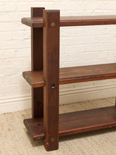 Load image into Gallery viewer, A three-tier wooden bookcase with a dark brown finish and brass corner hardware, set against a white brick wall and beige carpet.