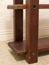 Load image into Gallery viewer, Close-up of a dark brown wooden table leg and shelf bracket, showing the wood grain, joinery, and a brass screw fastener, set against a white brick wall and beige rug.