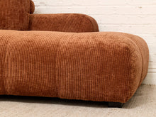Load image into Gallery viewer, A close-up of a rust-brown corduroy sofa with a ribbed fabric texture, set against a white brick wall and light-colored carpet.