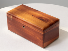 Load image into Gallery viewer, A rectangular wooden box with a glossy finish, showing natural wood grain and a small metal lock on the front, set on a white textured surface.
