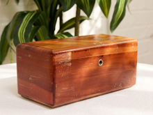 Load image into Gallery viewer, A rectangular vintage wooden box with a glossy reddish-brown finish and a small metal lock on the front, resting on a white textured surface with a blurred green plant in the background.