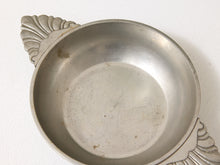 Load image into Gallery viewer, A vintage silver-toned metal bowl with decorative shell-shaped handles, shown from a top-down angle on a white textured fabric background.