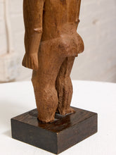 Load image into Gallery viewer, Close-up of a carved wooden figurine showing the back and buttocks of a nude human form, mounted on a dark rectangular wooden base against a light neutral background.