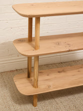Load image into Gallery viewer, A three-tier wooden shelving unit made from light natural pine wood, shown against a white brick wall and textured beige rug.
