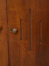 Load image into Gallery viewer, Close-up of a warm brown wooden cabinet door with vertical recessed handles, a round metal knob, and a keyhole.