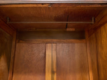 Load image into Gallery viewer, Close-up of a wooden storage cabinet or wardrobe interior with wood grain panels, a metal hanging rod, and a central pull handle.