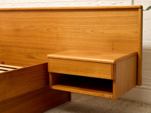 Load image into Gallery viewer, A close-up of a mid-century modern wooden bed frame with a floating nightstand and a tall headboard, made of warm honey-toned wood against a white brick wall.