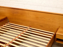 Load image into Gallery viewer, A close-up of a wooden bed frame with a slatted wooden mattress support base, set against a white brick wall.