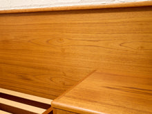 Load image into Gallery viewer, Close-up of a warm medium-brown wood grain surface, showing a tabletop corner, matching wooden slats, and a textured off-white wall in the background.