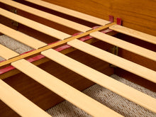 Load image into Gallery viewer, Close-up of a wooden bed frame slatted base with light natural wood slats over a medium brown wooden frame, with a textured beige rug visible underneath.