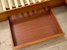 Load image into Gallery viewer, Close-up of a wooden drawer pulled open, showing a warm reddish-brown wood grain interior, with part of a matching wooden slatted frame visible above on a textured beige rug.