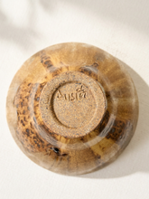 Load image into Gallery viewer, A top-down view of a handmade ceramic bowl with a brown and beige marbled glaze, showing the stamped brand name 'Austin' on the bottom, set against a neutral off-white background with soft shadows.
